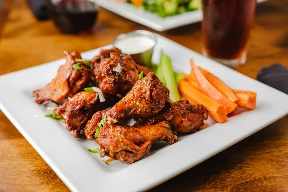 Plate of sauced chicken wings, celery, carrots, and dipping sauce.