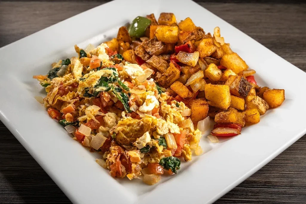 Scrambled eggs and roasted potatoes with mixed vegetables on a plate.