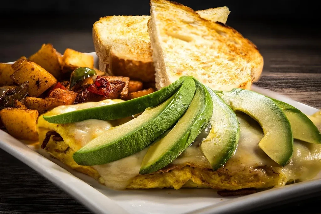 Close-up of plated brunch: cheesy eggs, fanned avocado, potatoes, and toast.