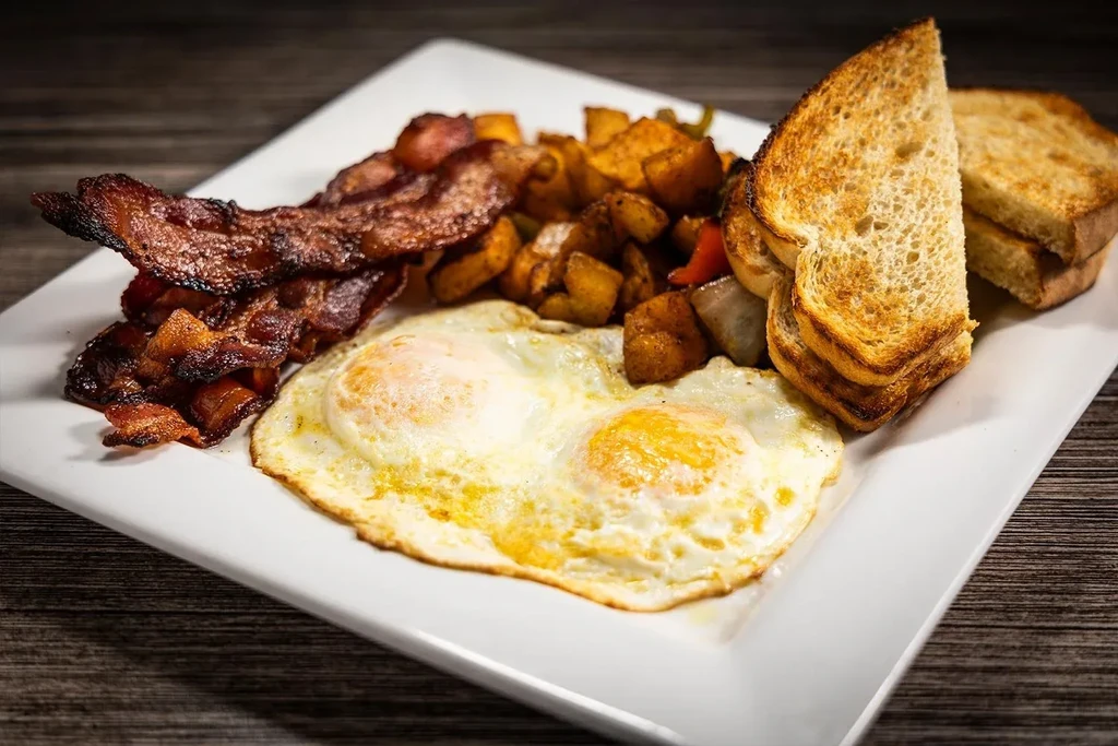 Rectangular plate with bacon, sunny-side eggs, home fries, and toast.