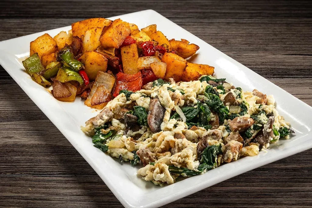 Top-down view: scrambled eggs with spinach, potato cubes and bell peppers.