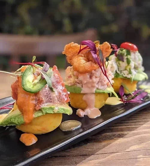 Three colorful plated appetizers featuring seafood on a black platter.
