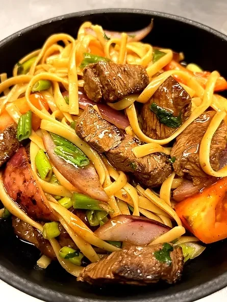 Top-down view of noodles, beef, and vegetables in a dark bowl.