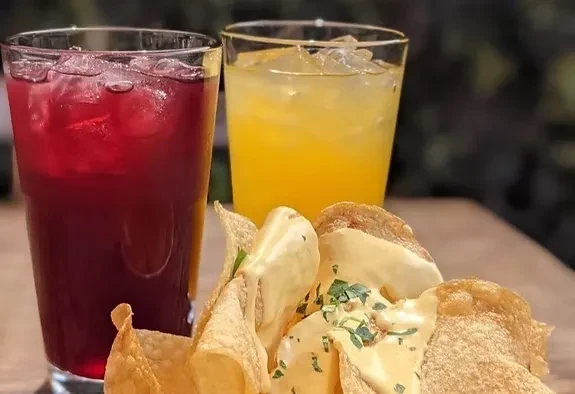 Two iced drinks and a plate of nachos with queso and herbs.