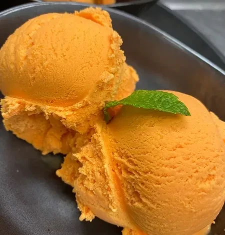 Bright orange ice cream scoops in dark bowl, topped with mint.