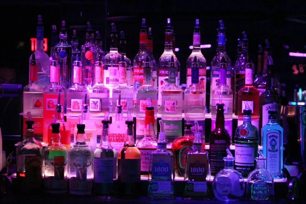 Colorful LED-lit liquor bottles on tiered shelves behind a bar.