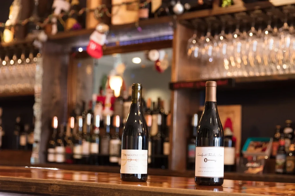 Two wine bottles on a bar counter in a festive bar.