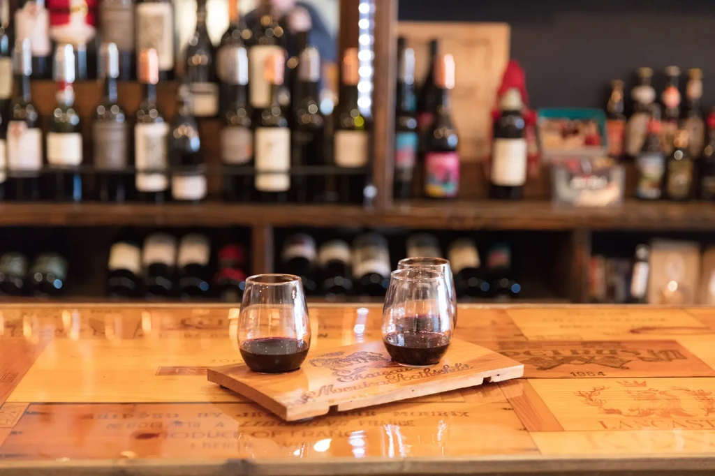 Red wine in two stemless glasses on a counter, blurred wine collection.