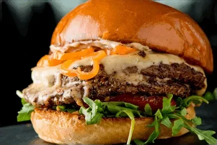Gourmet burger with two patties, melted cheese, orange pickles, and greens.
