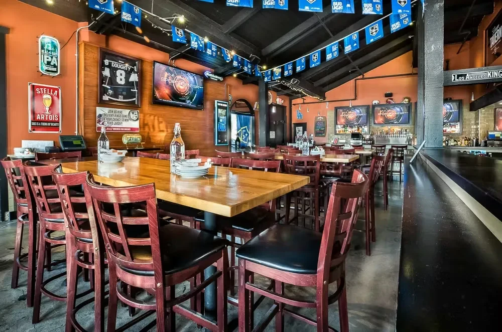Sports bar interior: communal table, TVs, hockey jersey, beer signs, bar.