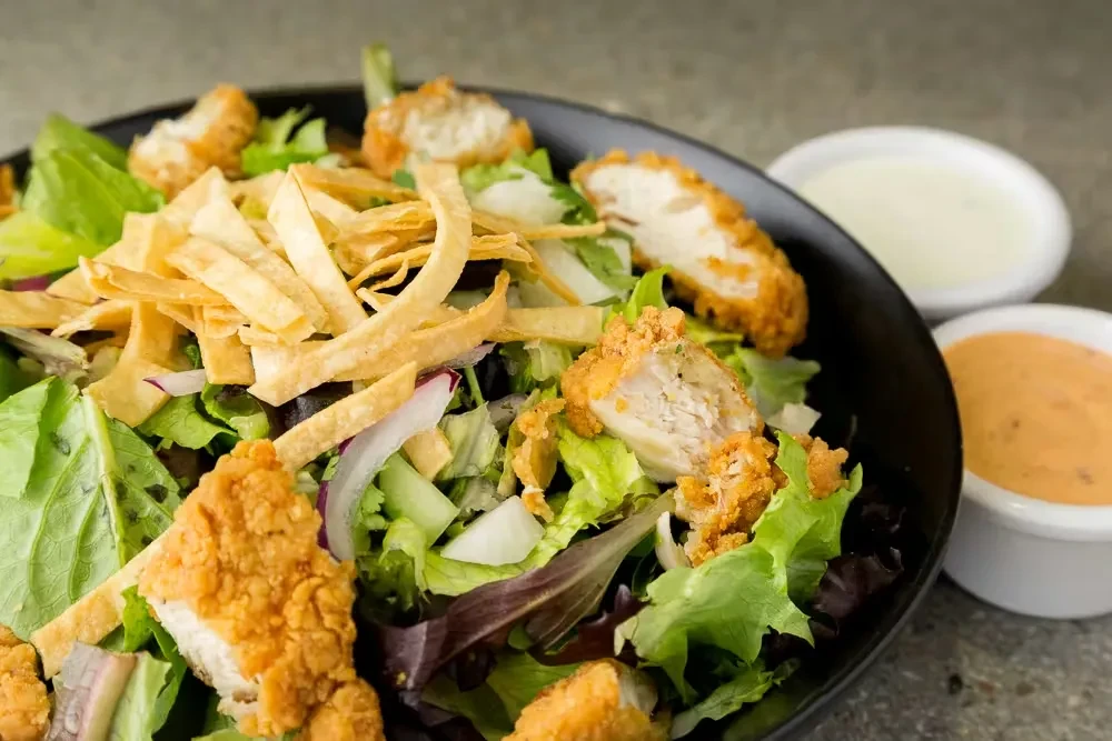 Fresh fried chicken salad with lettuce, tortilla strips, and sauces.