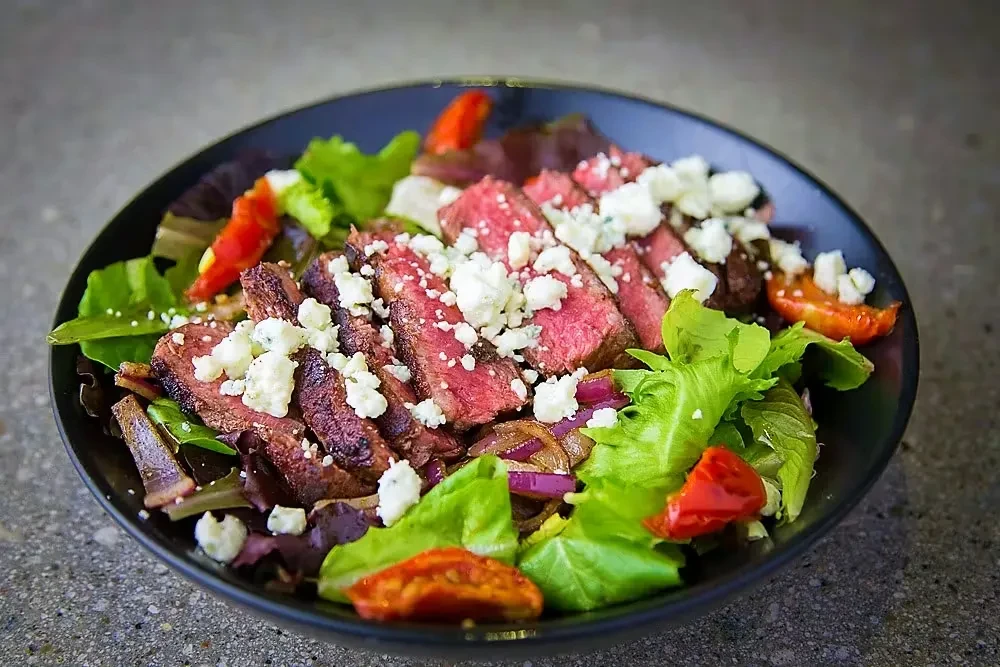 Steak salad with medium-rare steak, cheese, lettuce, and roasted vegetables.