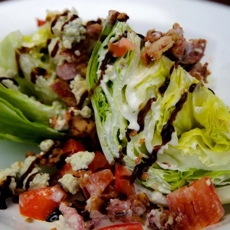 Classic wedge salad with blue cheese, bacon, tomatoes, and balsamic drizzle.