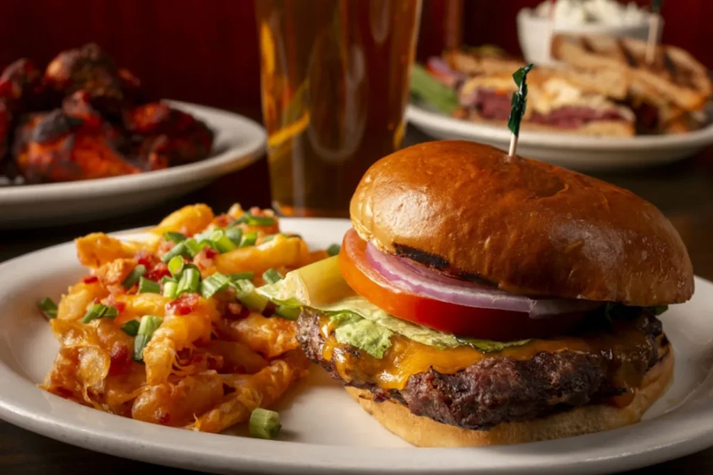 Close-up: Cheeseburger, fries topped with cheese, bacon, green onions.