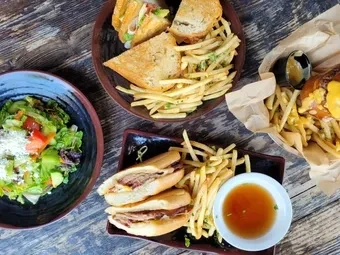 Overhead shot of multiple sandwiches, fries, and salad on a wooden table.