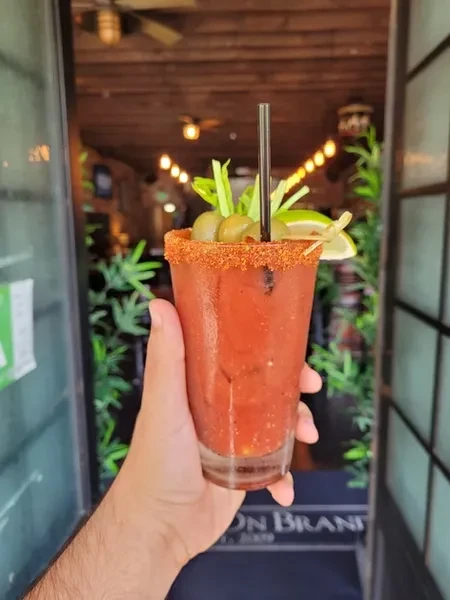 A hand holds a garnished Bloody Mary cocktail with a spiced rim.