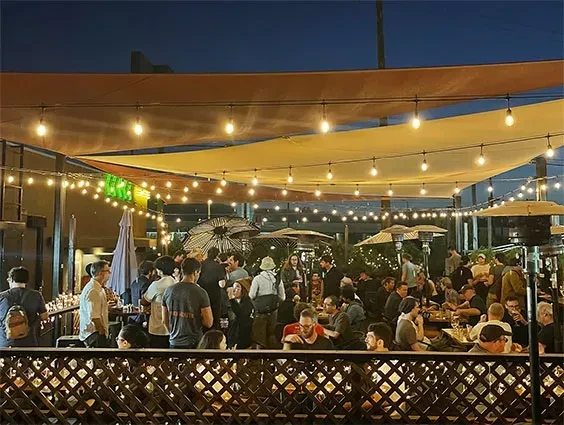 Crowded outdoor bar at night, illuminated by string lights and heaters.