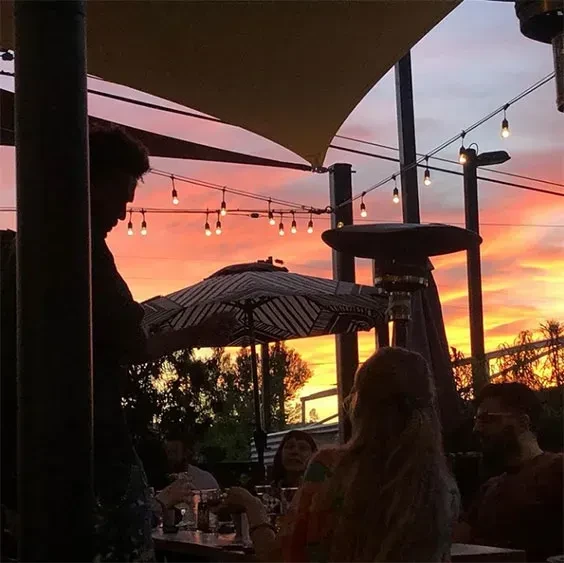 Outdoor dining area at sunset with string lights and silhouetted patrons.