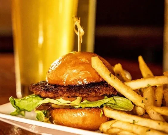 Gourmet burger, golden fries, and beverage on a rectangular white plate.
