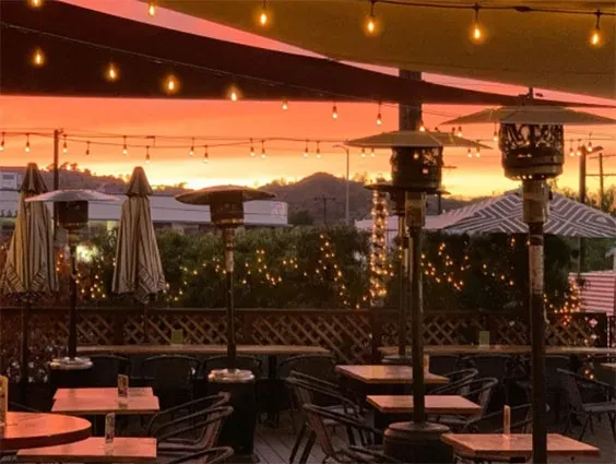 Empty outdoor dining patio with heaters and string lights at sunset.