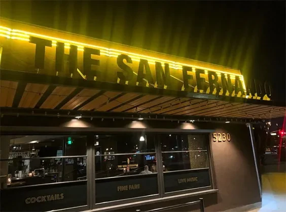 Exterior of The San Fernando restaurant at night with bright yellow neon sign.