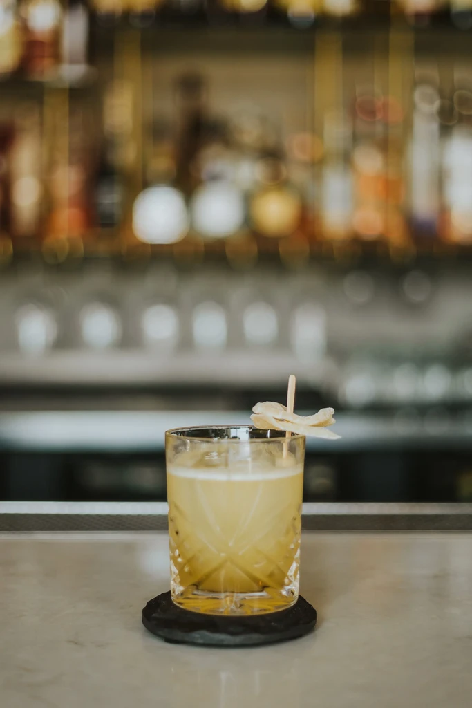Frothy light yellow cocktail with garnish on a bar.