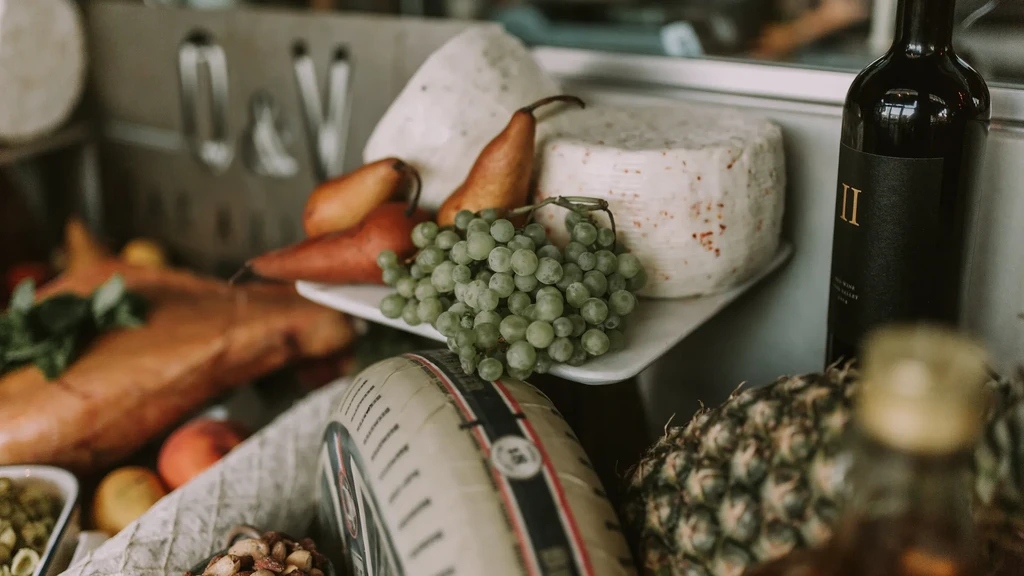 Artisanal cheese, grapes, pears, wine, and cured meat on a platter.