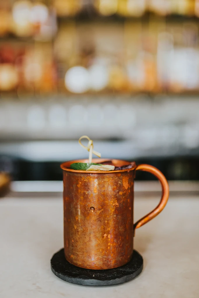 Copper mug with lime and citrus garnish, on a dark coaster.