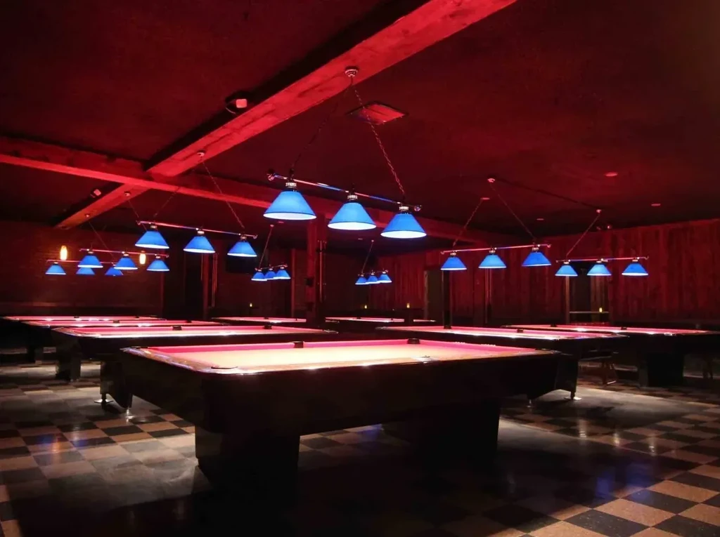 Dark, moody room with pool tables lit by red and blue light.