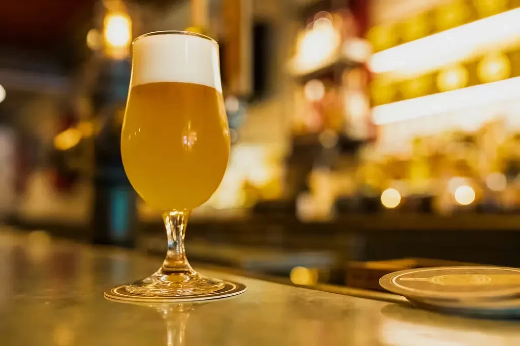 A stemmed glass of golden beer with foam on a bar.