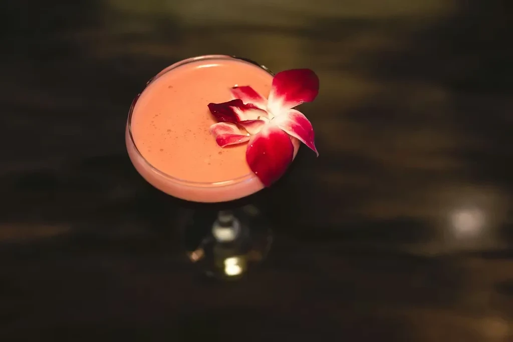 Creamy peach cocktail in coupe glass, garnished with a red orchid.