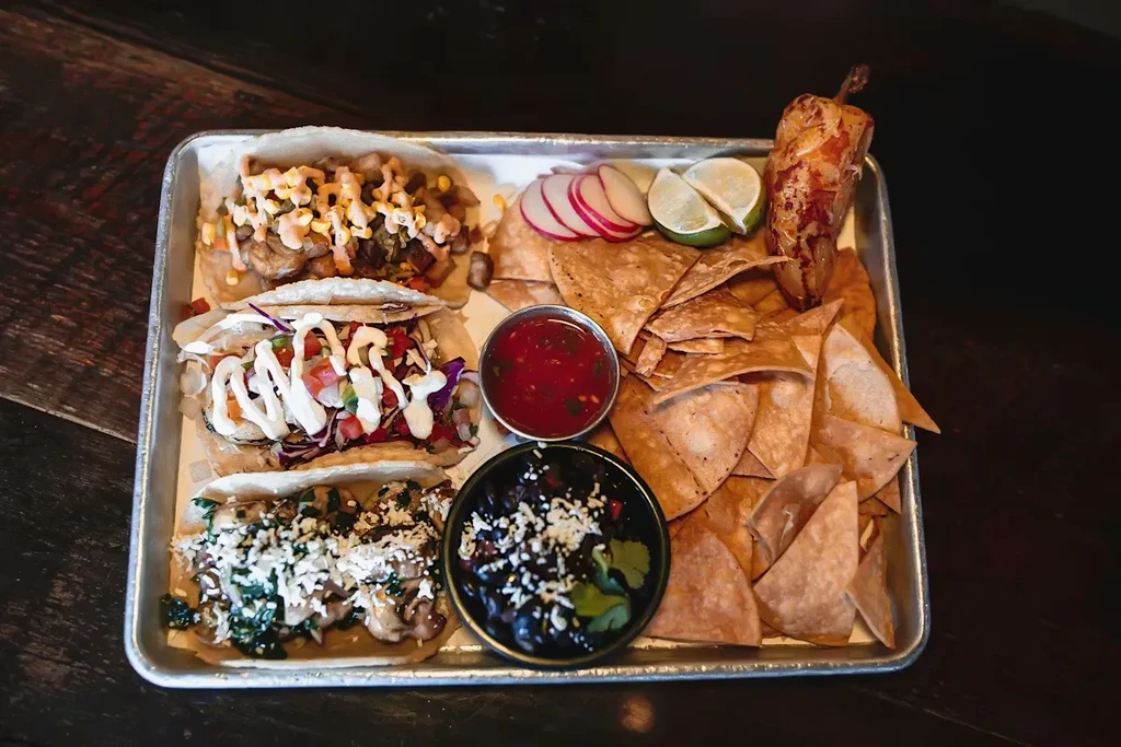 Platter of Mexican tacos, chips, salsa, beans, and limes on a tray.