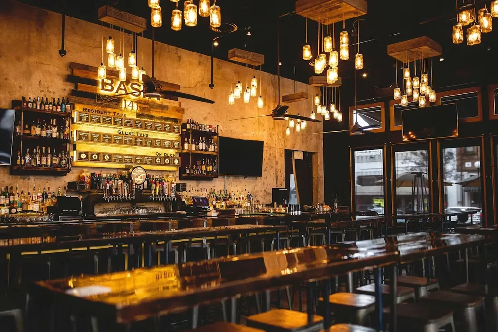 Empty industrial-chic bar with "BASIN 141" sign, beer taps, and liquor.