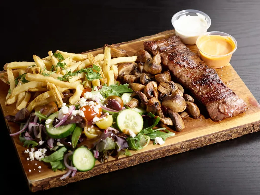 Grilled steak with mushrooms, fries, and salad on a rustic plank.