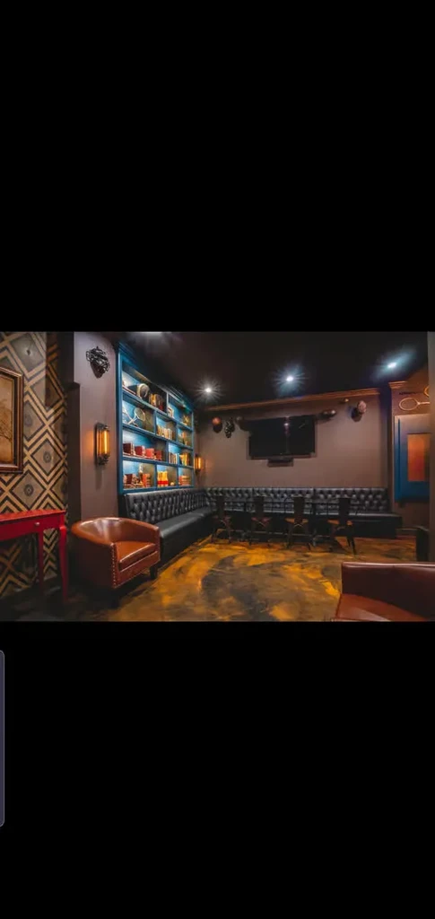 Stylish lounge with geometric wallpaper, blue-lit bookshelf, and tufted booth seating.