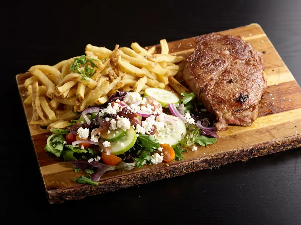 Grilled steak, french fries, and fresh salad on a wooden board.