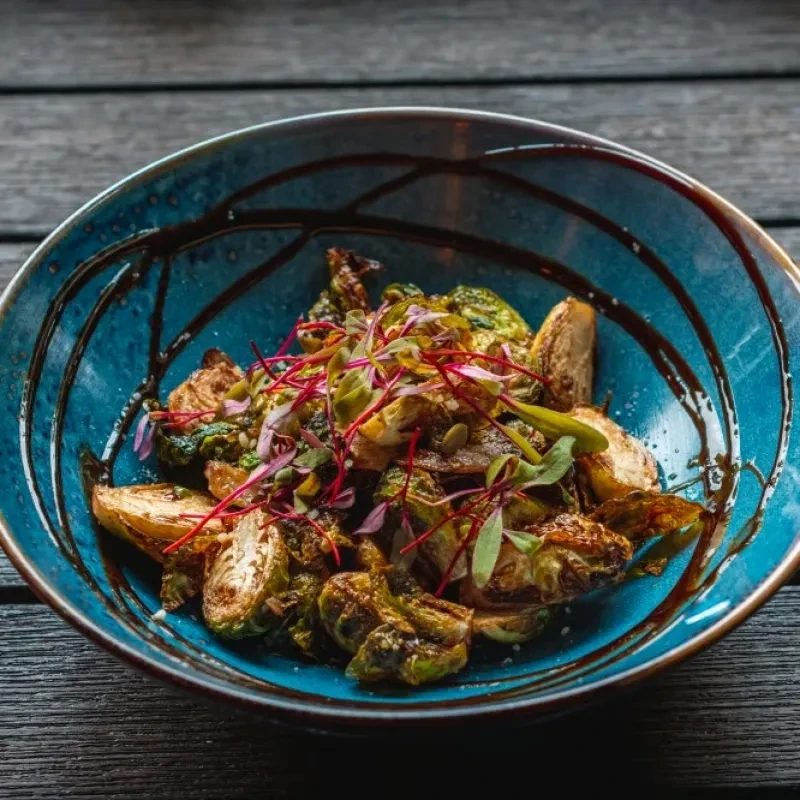 Roasted Brussels sprouts and potatoes with microgreens in a blue bowl.
