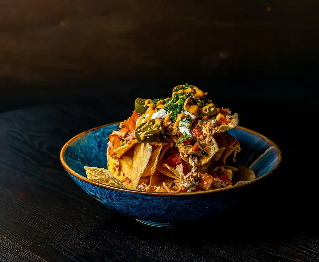Loaded blue bowl of nachos with meat, cheese, tomatoes, jalapeños, cilantro.
