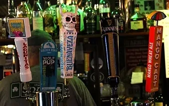 Five distinct beer taps in a dim bar, with a bartender.