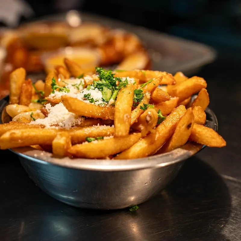 Golden-brown french fries topped with white cheese and green herbs.