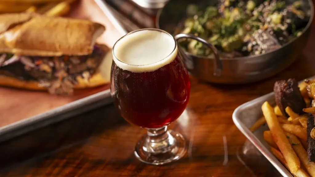 Dark beer, sandwich, french fries, and salad on a wooden table.