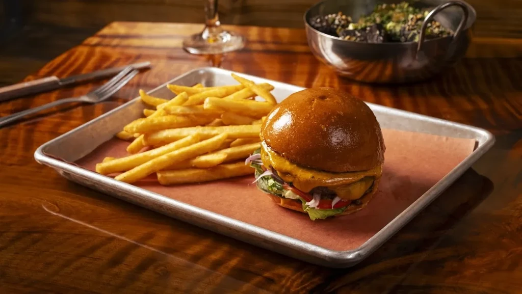 Burger and golden fries on a metal tray on a wooden table.