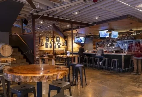 Industrial-style bar interior with exposed pipes, concrete, and wooden furnishings.