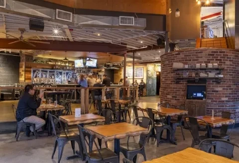 Spacious industrial-rustic brewpub interior with lively bar, tables, and brick oven.