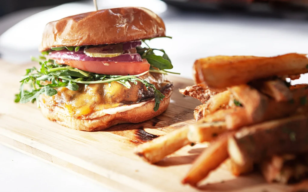Cheeseburger with fresh toppings and thick-cut fries on a wooden board.