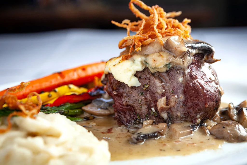 Plated seared meat with creamy sauce, fried onions, vegetables, and mashed potatoes.