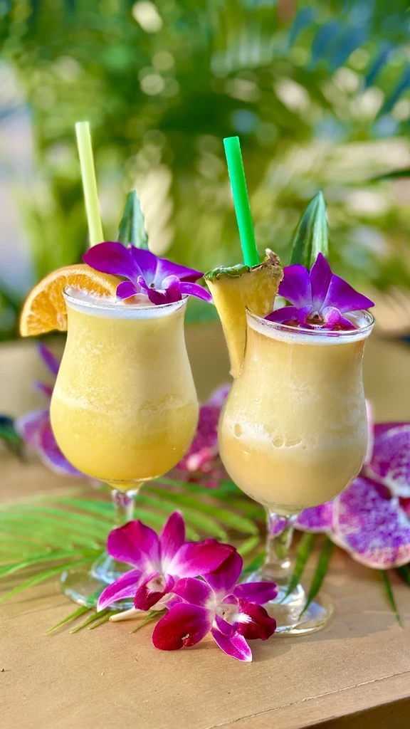 Tropical frozen cocktails with orchid, orange, and pineapple garnishes.