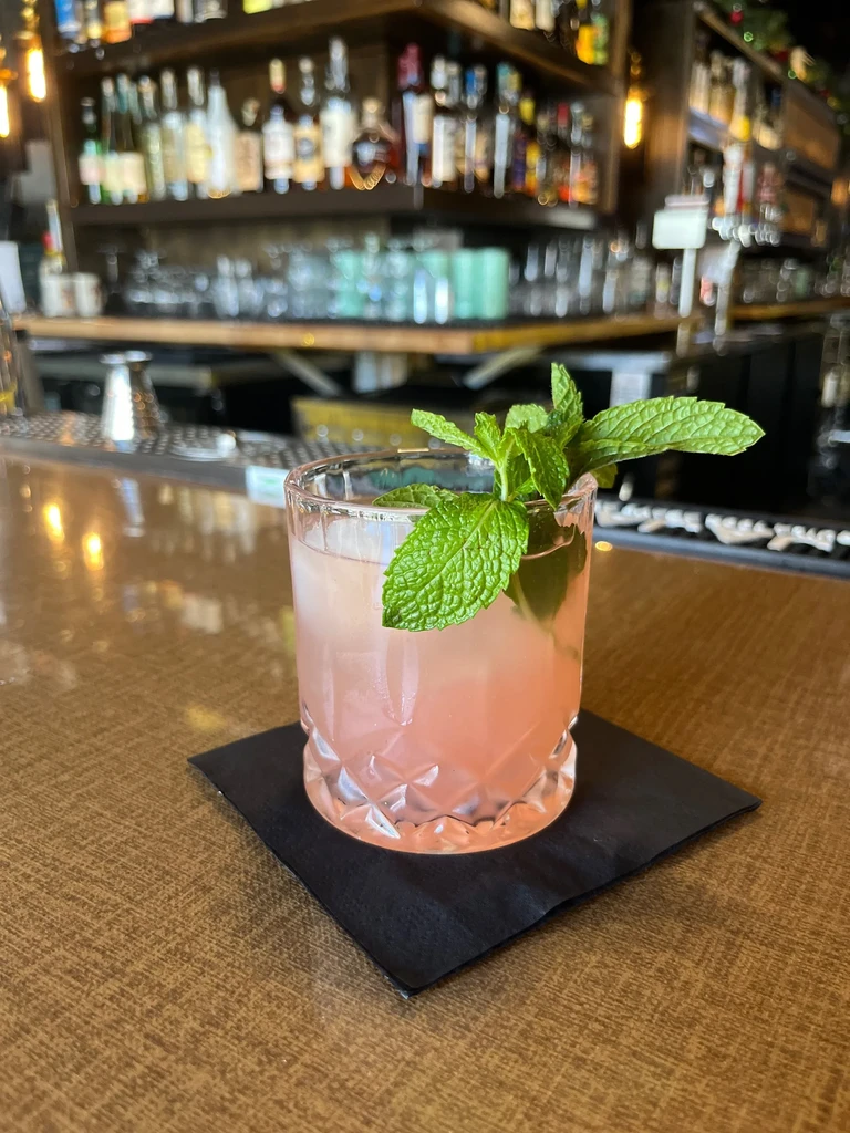 Light pink cocktail with mint in faceted glass on bar.