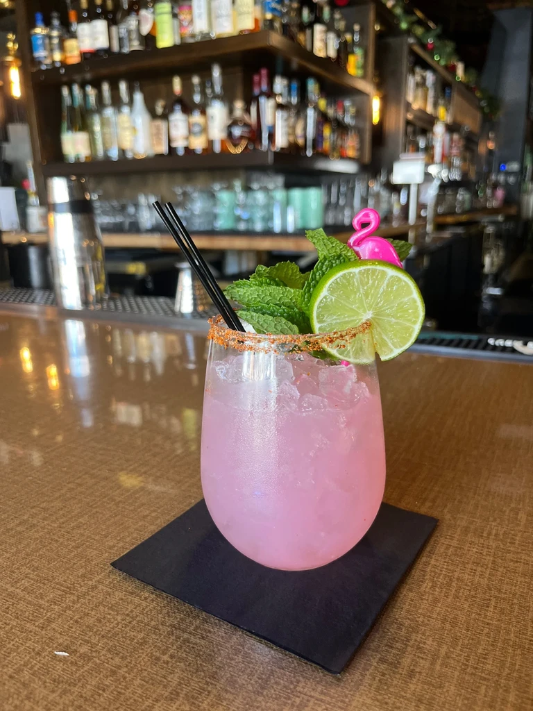 Pink cocktail, chili-lime rim, mint, lime, flamingo stirrer, on bar.