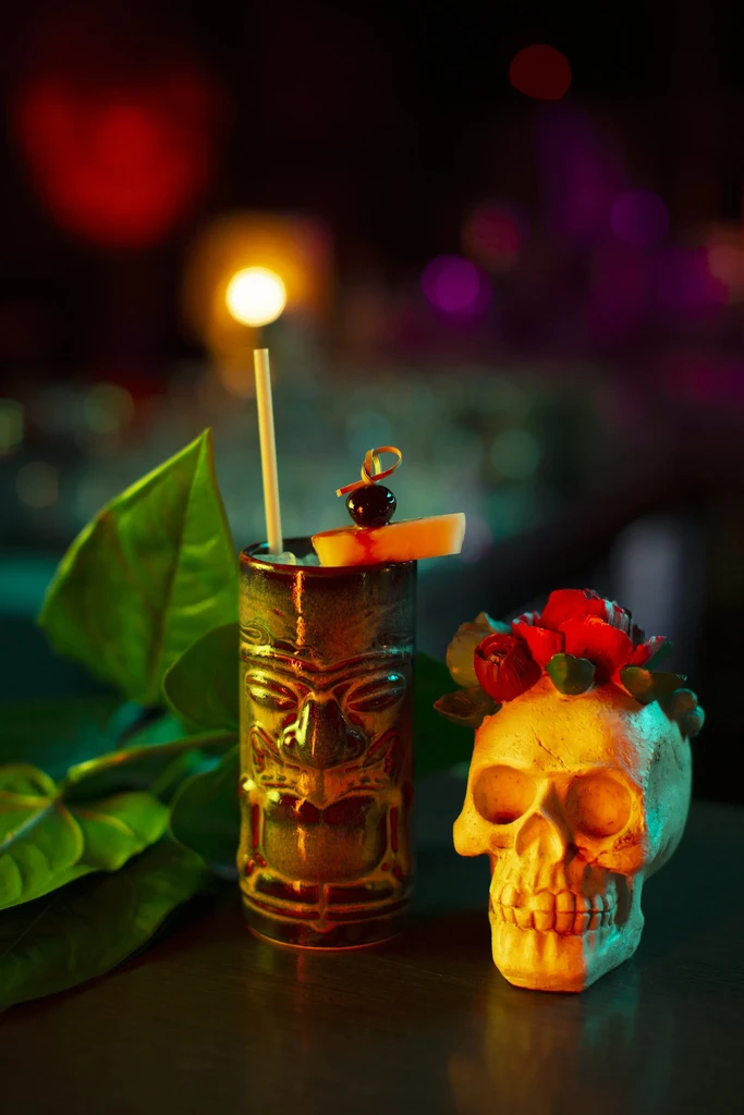 A tiki cocktail and a rose-adorned skull in moody lighting.